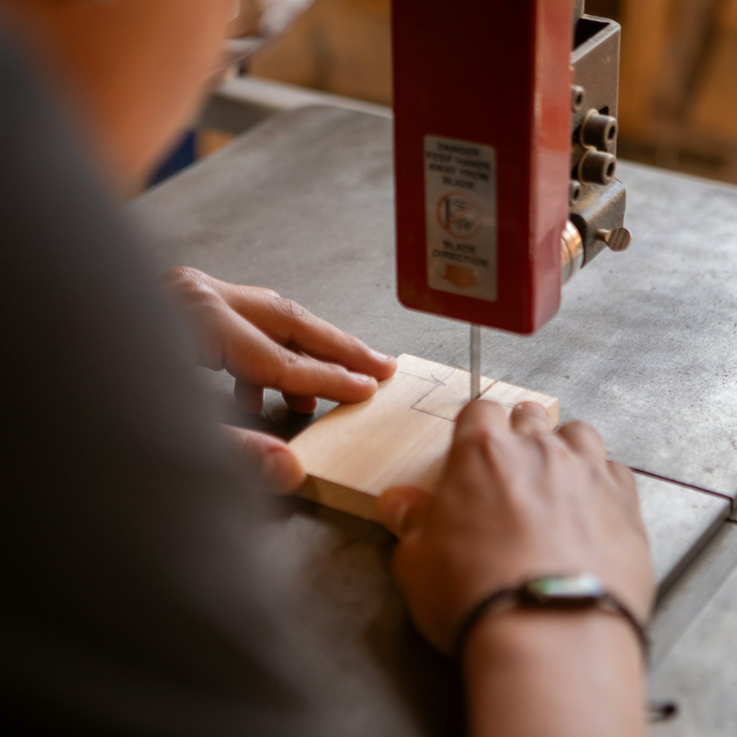Hands guide a piece of wood through a band saw.
