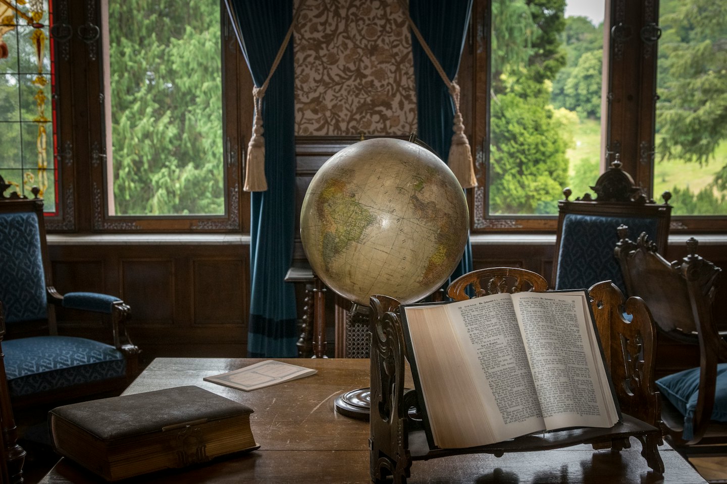 Ornate wooden desk with a globe and books in a study.